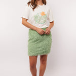 Model draagt de mintgroene Arianne Skirt van Fluresk met een wit T-shirt en oranje sneakers, perfect voor een zomerse casual look.