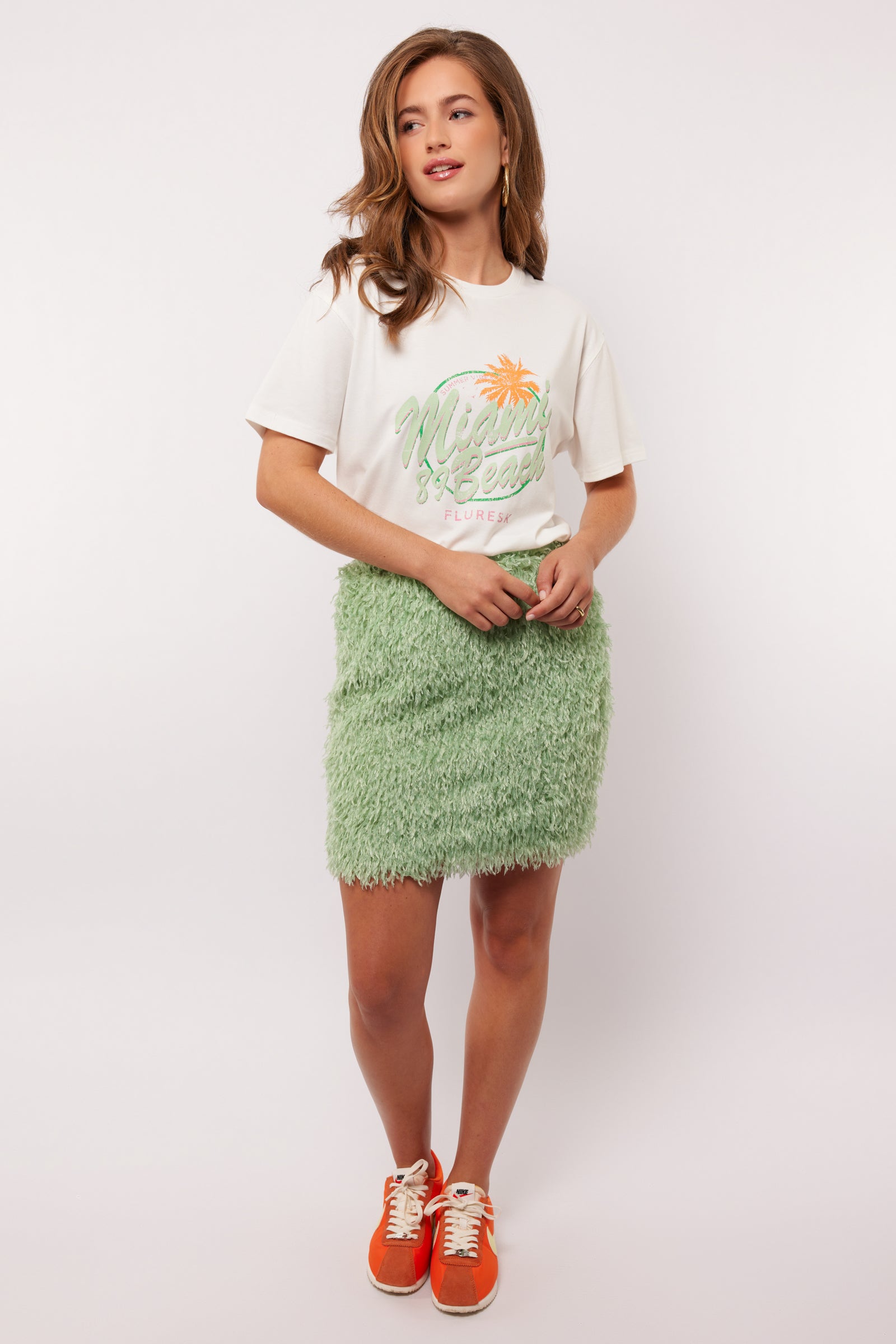 Model draagt de mintgroene Arianne Skirt van Fluresk met een wit T-shirt en oranje sneakers, perfect voor een zomerse casual look.
