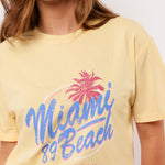 Pastelgeel T-shirt met roze-blauwe Miami 89 Beach print van Fluresk – zomerse vibes gegarandeerd.