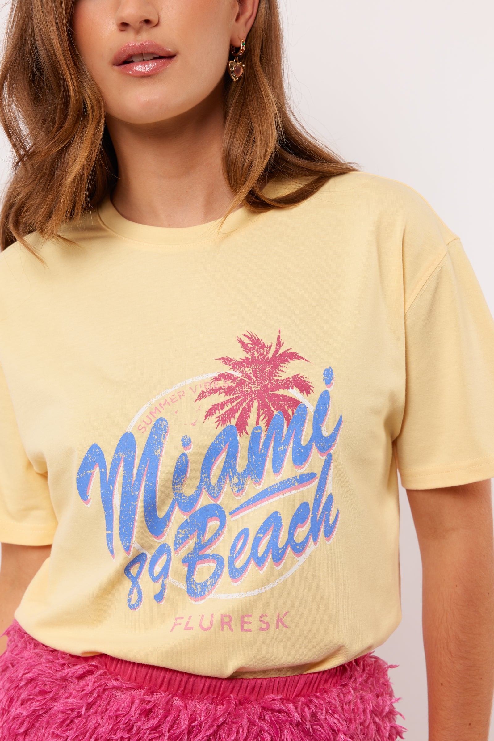 Pastelgeel T-shirt met roze-blauwe Miami 89 Beach print van Fluresk – zomerse vibes gegarandeerd.