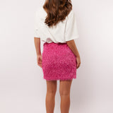 Model van achteren met de roze Arianne skirt van Fluresk, gecombineerd met een oversized wit shirt en sneakers.