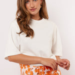 Model draagt het witte Fluresk Brix T-shirt in een casual outfit met een oranje bloemenrok en gouden oorbellen.