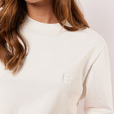 Detail van het witte Fluresk Brix T-shirt met ton-sur-ton geborduurd logo op de borst en subtiele ronde hals.