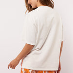 Model draagt het Fluresk Brix T-shirt van achteren, losjes gestyled over een opvallende bloemenrok.