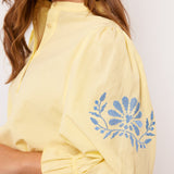 Detail van gele Fluresk blouse met blauwe bloemenborduursel op pofmouw.