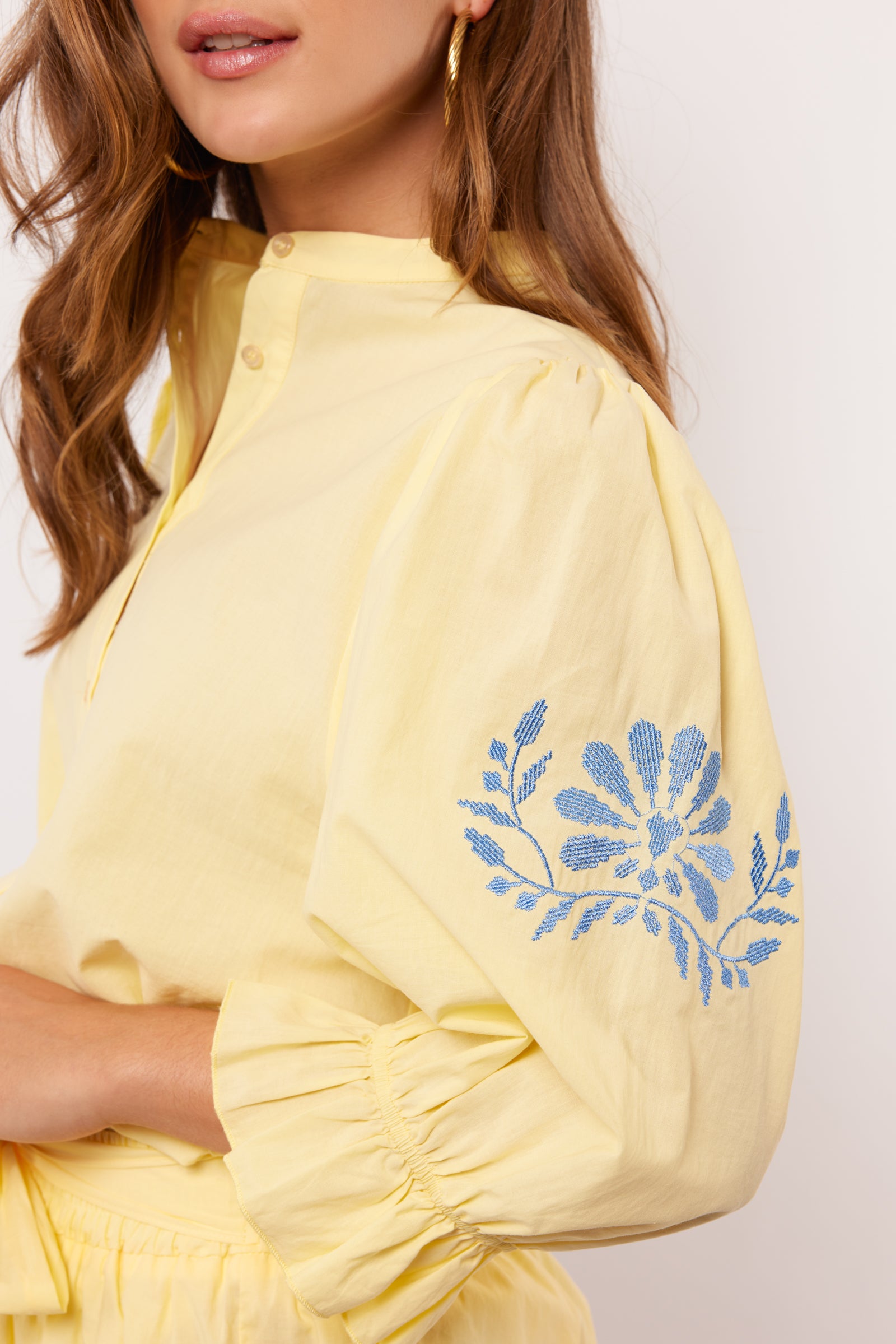 Detail van gele Fluresk blouse met blauwe bloemenborduursel op pofmouw.