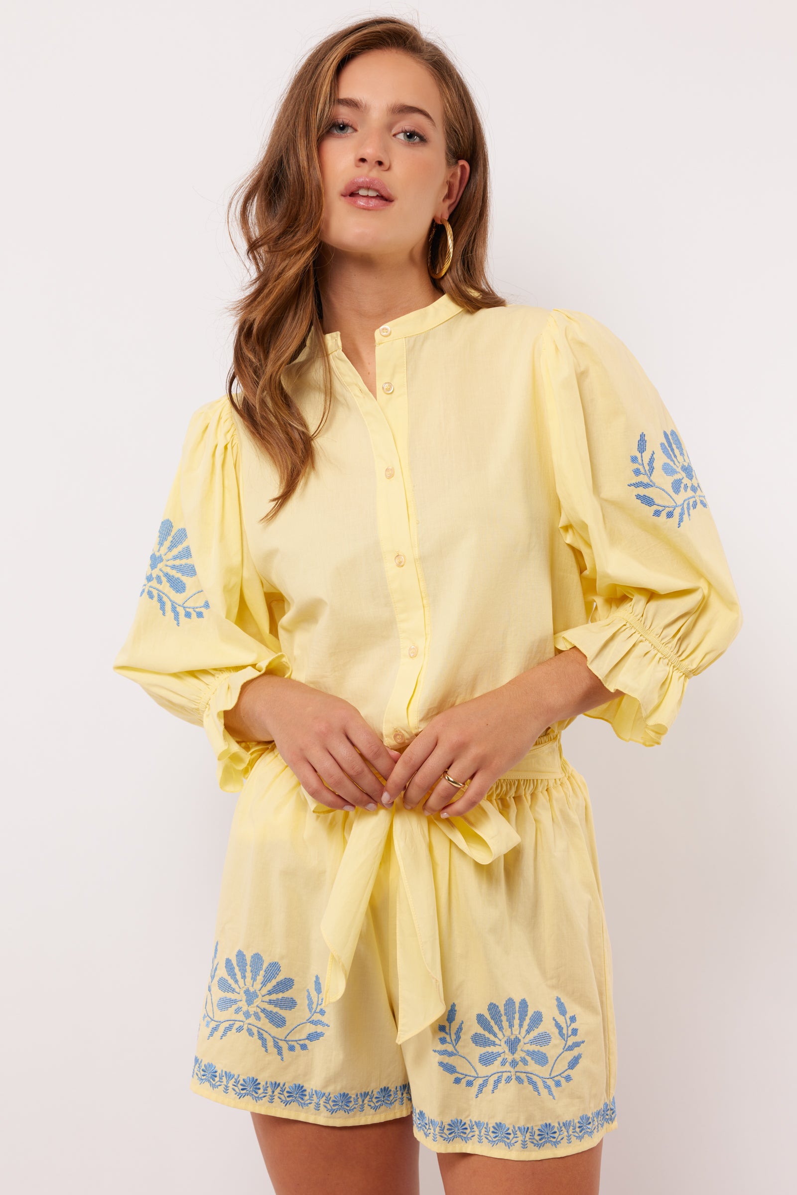 Model draagt gele Fluresk Marlowe blouse met bijpassende short en blauwe borduursels.