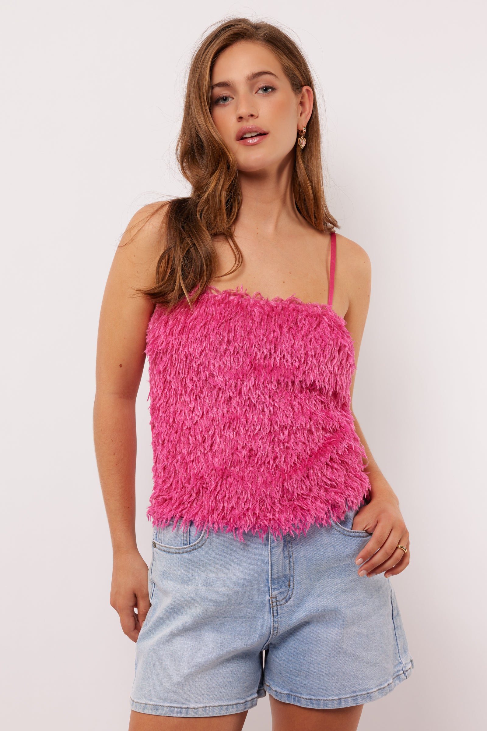 Vrouw draagt de Millicent top in felroze met fluffy textuur aan de voorkant en denim short, voor een speelse zomerse look.