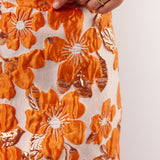 Detailopname van de oranje bloemenprint op de Mindy Skirt van Fluresk, met glanzende afwerking en zichtbare textuur.