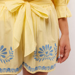 Close-up van de gele Fluresk Saine short met blauwe borduursels en strikceintuur in de taille.