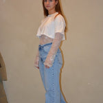 Model draagt een lichtblauwe jeans met een rechte pasvorm en subtiele wassing, gestyled met een witte cropped top en kanten details voor een trendy look.