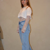 Model draagt een lichtblauwe jeans met een rechte pasvorm en subtiele wassing, gestyled met een witte cropped top en kanten details voor een trendy look.