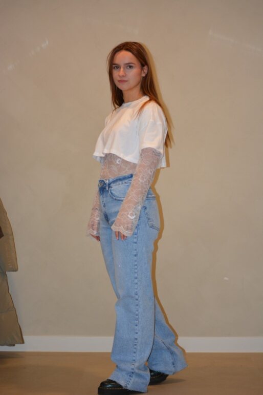 Model draagt een lichtblauwe jeans met een rechte pasvorm en subtiele wassing, gestyled met een witte cropped top en kanten details voor een trendy look.
